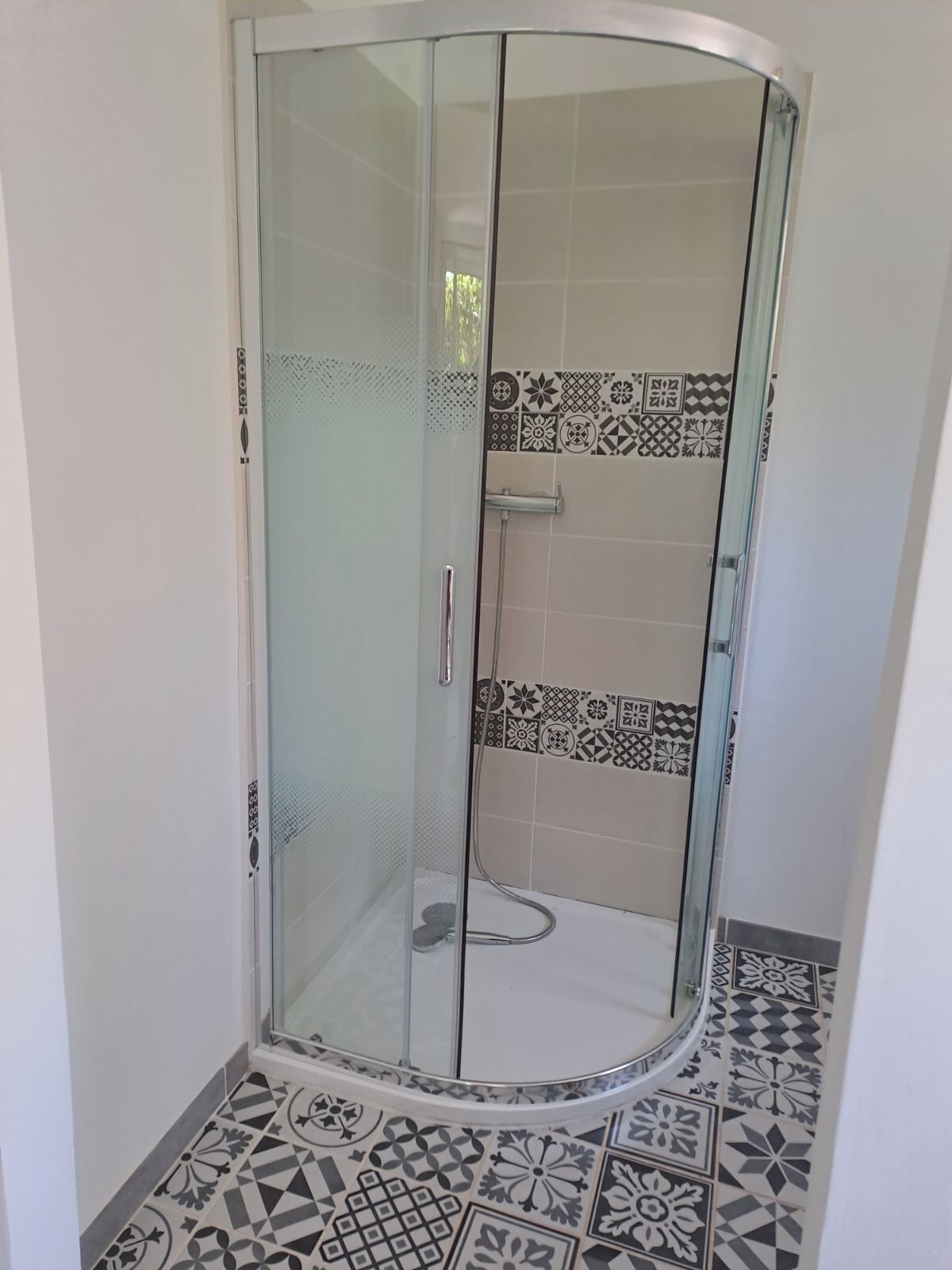 A glass-enclosed shower with a white tiled floor and walls.