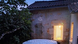 A hot tub in a garden with a wooden deck leading to a stone building. - Au Doux Rêves (Corgnac-sur-l'Isle)