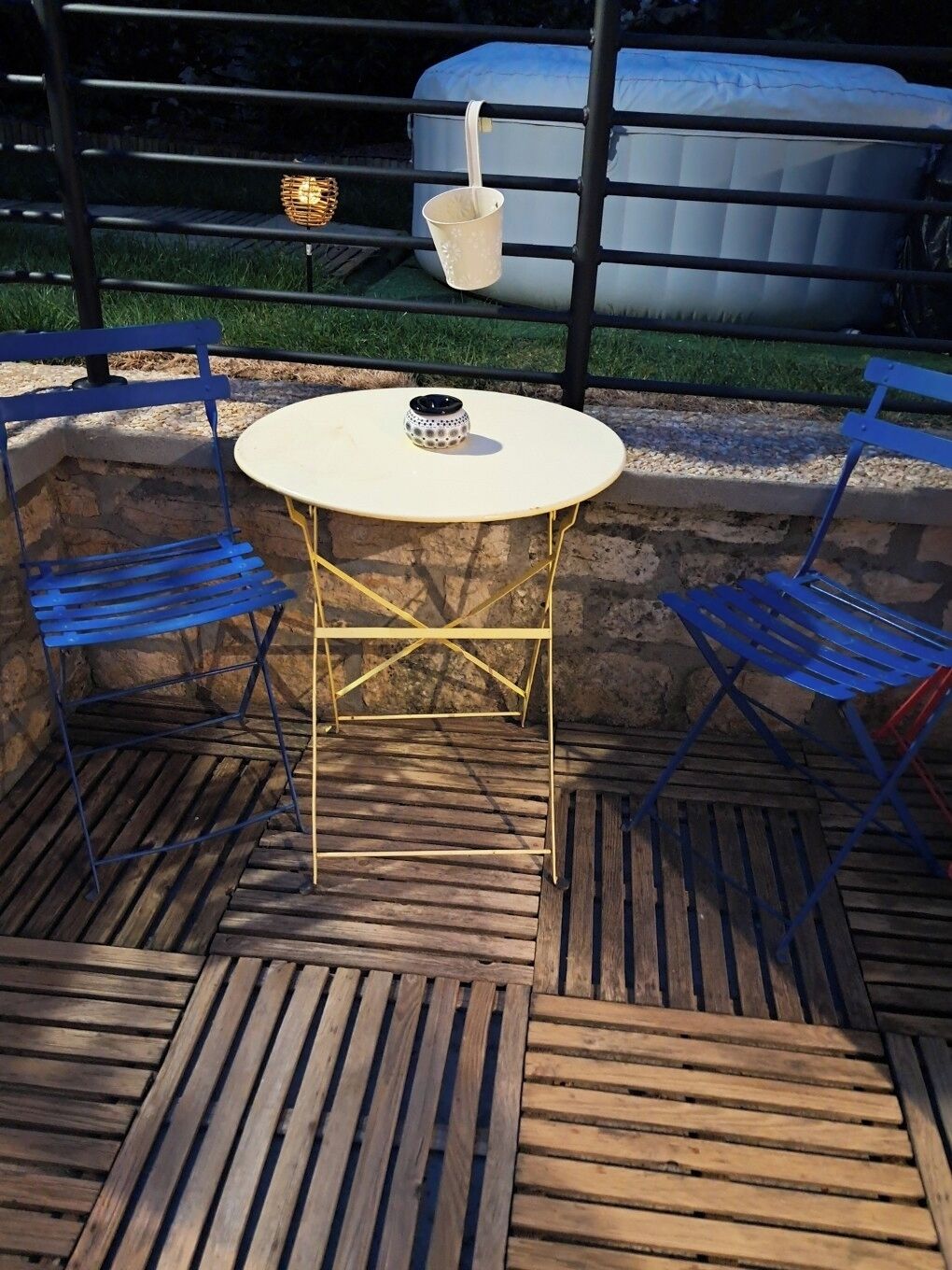 A patio with a round table and blue chairs, a white bucket, and a wicker basket.