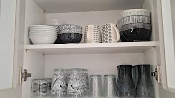 Un meuble de cuisine contenant divers ustensiles, notamment des saladiers, des assiettes et des bocaux en verre.
