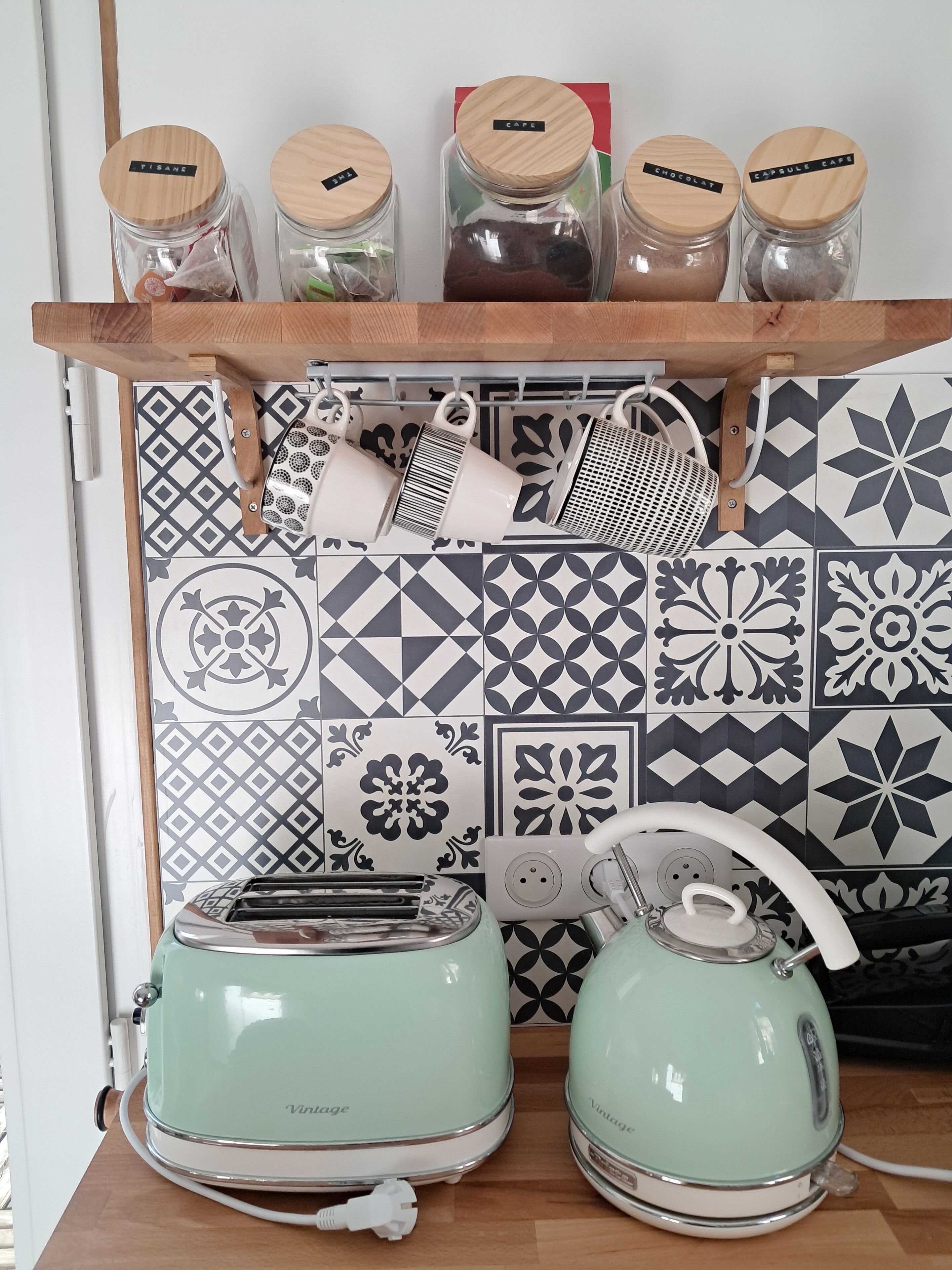 Una cocina con dos tostadoras de estilo vintage, una tetera y frascos etiquetados con ingredientes como 'TISANE' y 'CHOCOLAT'.