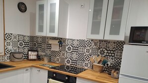 A kitchen with white cabinets, a black stove, and patterned backsplash tiles. - Au Doux Rêves (Corgnac-sur-l'Isle)