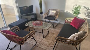 Een moderne woonkamer met rieten meubels, een glazen bijzettafeltje en een televisie.