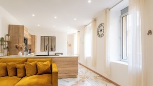 A modern living room with a sofa, a kitchen area, and a large window. - Sauna Hammam Terrasse Hyper Centre (Nîmes)