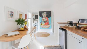 A modern kitchen with a wooden countertop, a coffee machine, and a sink. There is a dining area with a table and chairs, and a large painting on the wall. - Idlewild Studio: Scandinavian studio just 20min to uptown (Matthews)