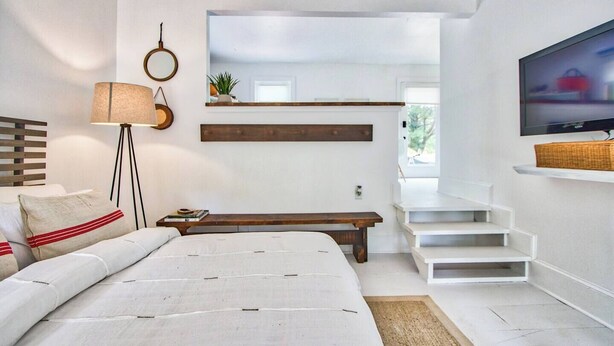 A modern bedroom with a bed, a bedside table, a lamp, a mirror, a TV, and a staircase leading to another room. - Idlewild Studio: Scandinavian studio just 20min to uptown (Matthews)