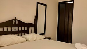 A neatly made bed with white linens, a wooden headboard, a bedside table, a mirror, and a door.