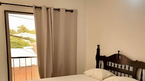 A bedroom with a bed, curtains, and a view of the outdoors.