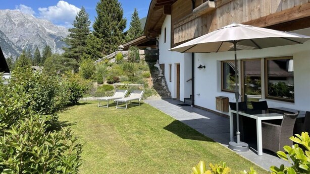 Un moderno chalet con zona de patio, mobiliario exterior y un paisaje de montaña al fondo.