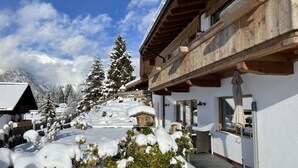 Un edificio cubierto de nieve con un balcón de madera y vistas a árboles y montañas nevadas.