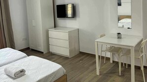 Habitación de hotel con cama, escritorio con silla, armario, televisor y espejo.