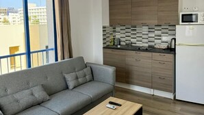 Una sala moderna con un sofá gris, una mesa de centro de madera y una cocina con armarios de madera y un microondas.