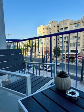 Un balcon avec une balustrade bleue, une chaise noire, un pot de fleurs et une petite table.