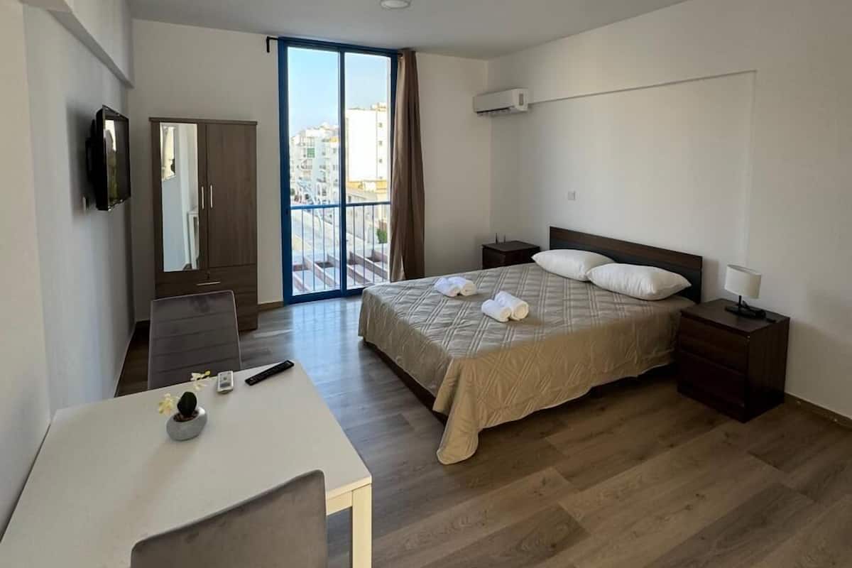 A modern hotel room with a bed, bedside table, and a desk with a chair.