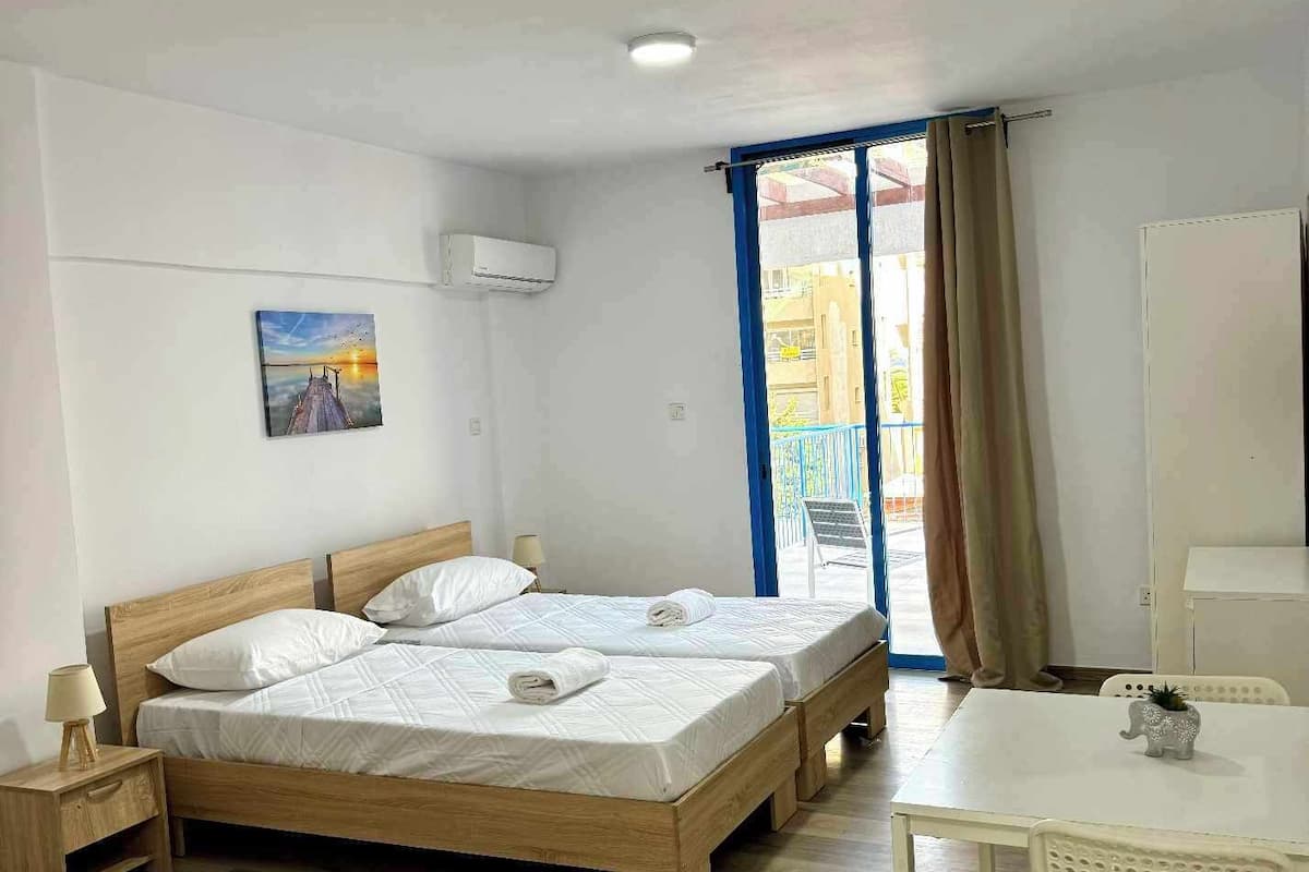 A room with two wooden beds, a white table with a chair, and a painting on the wall.