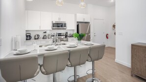 Una cocina moderna con armarios blancos, electrodomésticos de acero inoxidable y una isla central con taburetes de bar.