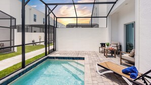 Un área de piscina moderna al aire libre con cerramiento de vidrio, una silla de descanso y una pequeña mesa con una planta.