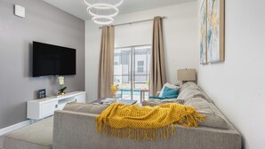 Una sala de estar moderna con una televisión de pantalla plana, un sofá, un plaid amarillo y un ventanal con cortinas.