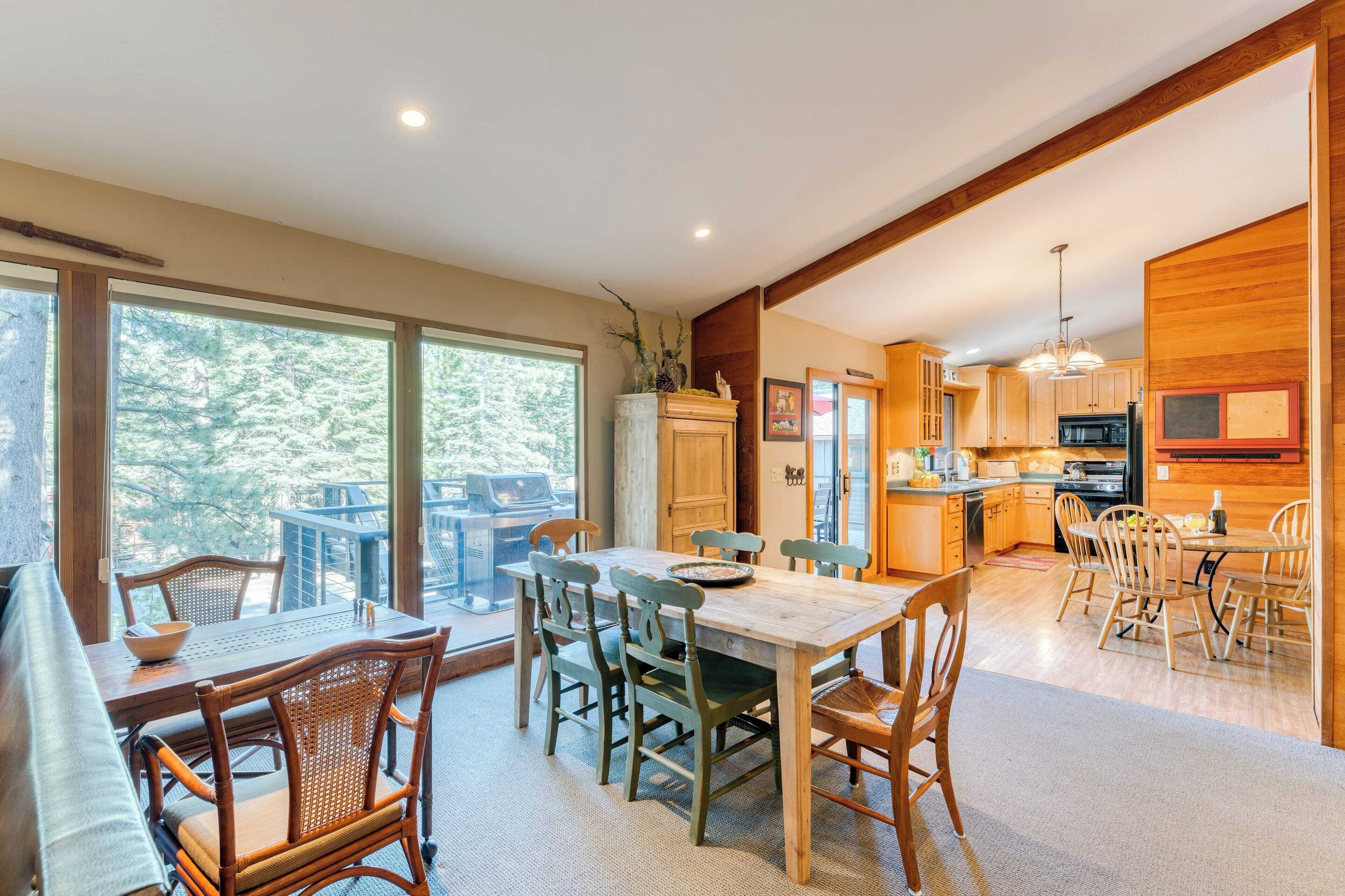 Una cocina amplia con armarios de madera y una isla grande, un comedor con mesa y sillas de madera, y ventanas grandes que ofrecen vistas al exterior.