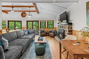 A spacious living room with a large sofa, a wooden coffee table, and a fireplace. There are multiple windows providing natural light and views of the outdoors. - Summit Shores Tranquil Escape Designed for Groups w/ Hot Tub, Fire Pit + Game Room (Lake Harmony)