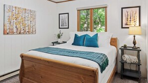 A neatly arranged bedroom with a wooden bed, a bedside table with a lamp, and artwork on the walls.