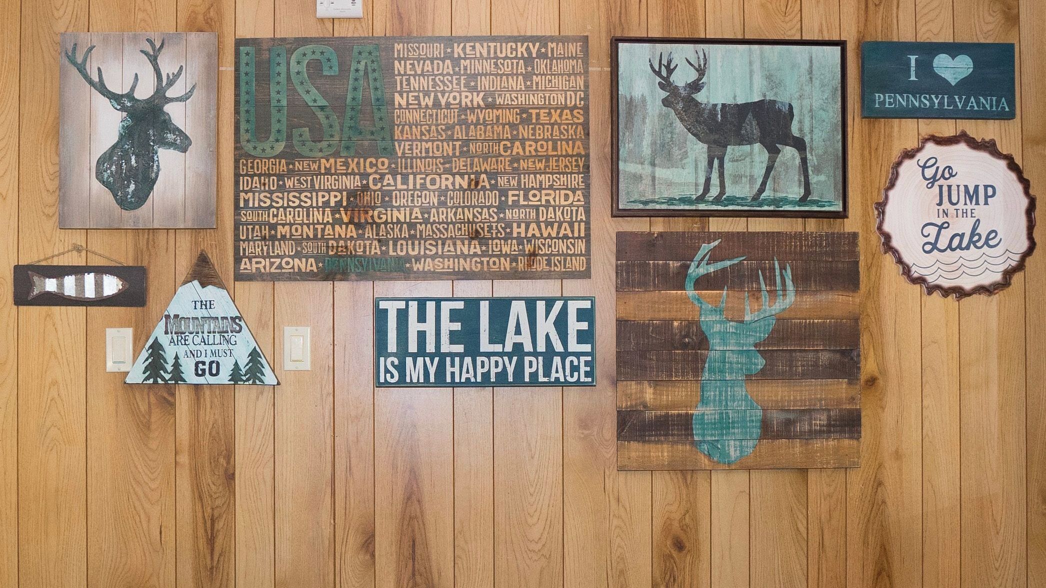 A wooden wall with various signs and decorations, including a sign listing U.S. states, a deer silhouette, and a sign that says 'I love Pennsylvania.'