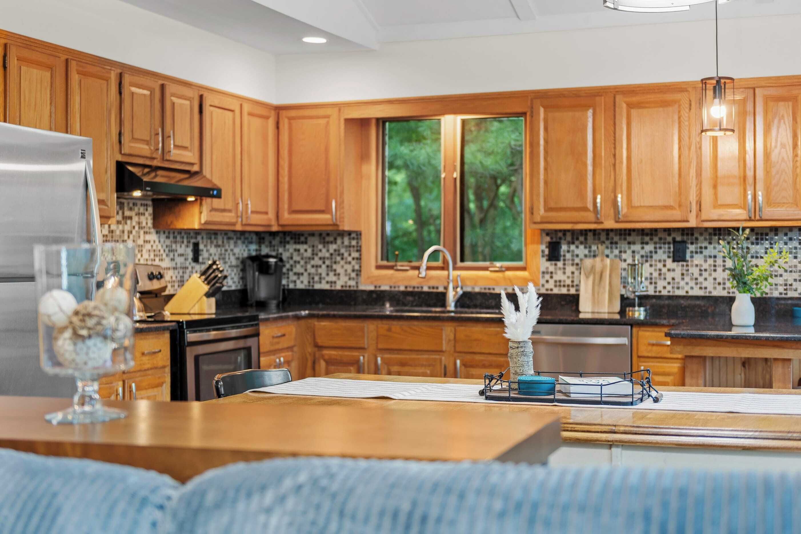 A modern kitchen with wooden cabinets, a black countertop, and a window with a view of trees.