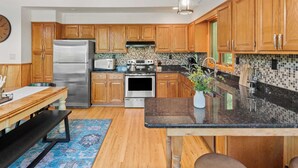 A modern kitchen with wooden cabinets, stainless steel appliances, a black granite countertop, and a blue patterned rug.