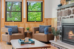 A cozy living room with two leather sofas, a coffee table, and a stone fireplace. - Summit Shores Tranquil Escape Designed for Groups w/ Hot Tub, Fire Pit + Game Room (Lake Harmony)