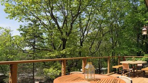 A wooden deck with round tables and chairs, surrounded by lush green trees.