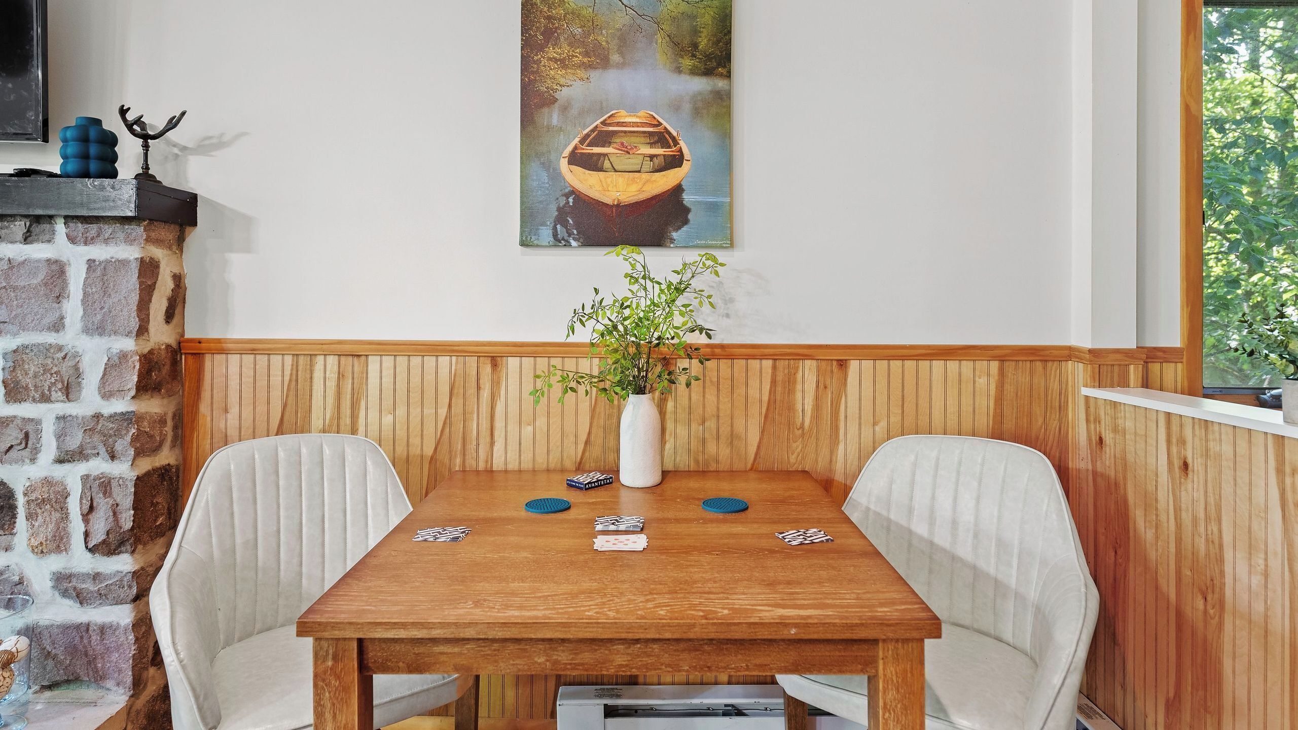 Una mesa de comedor con sillas, un florero con plantas verdes y cartas sobre la mesa.