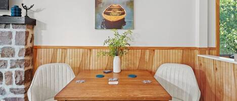 Una mesa de comedor con sillas, un florero con plantas verdes y cartas sobre la mesa.