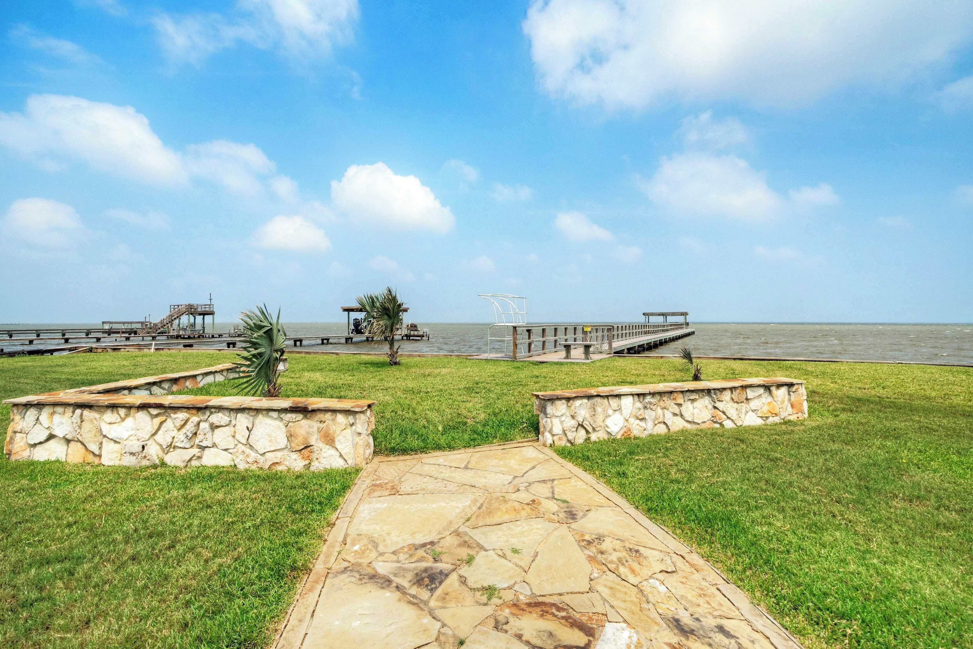 A stone pathway leading to a waterfront area with a view of the sea, a small palm tree, and a gazebo.