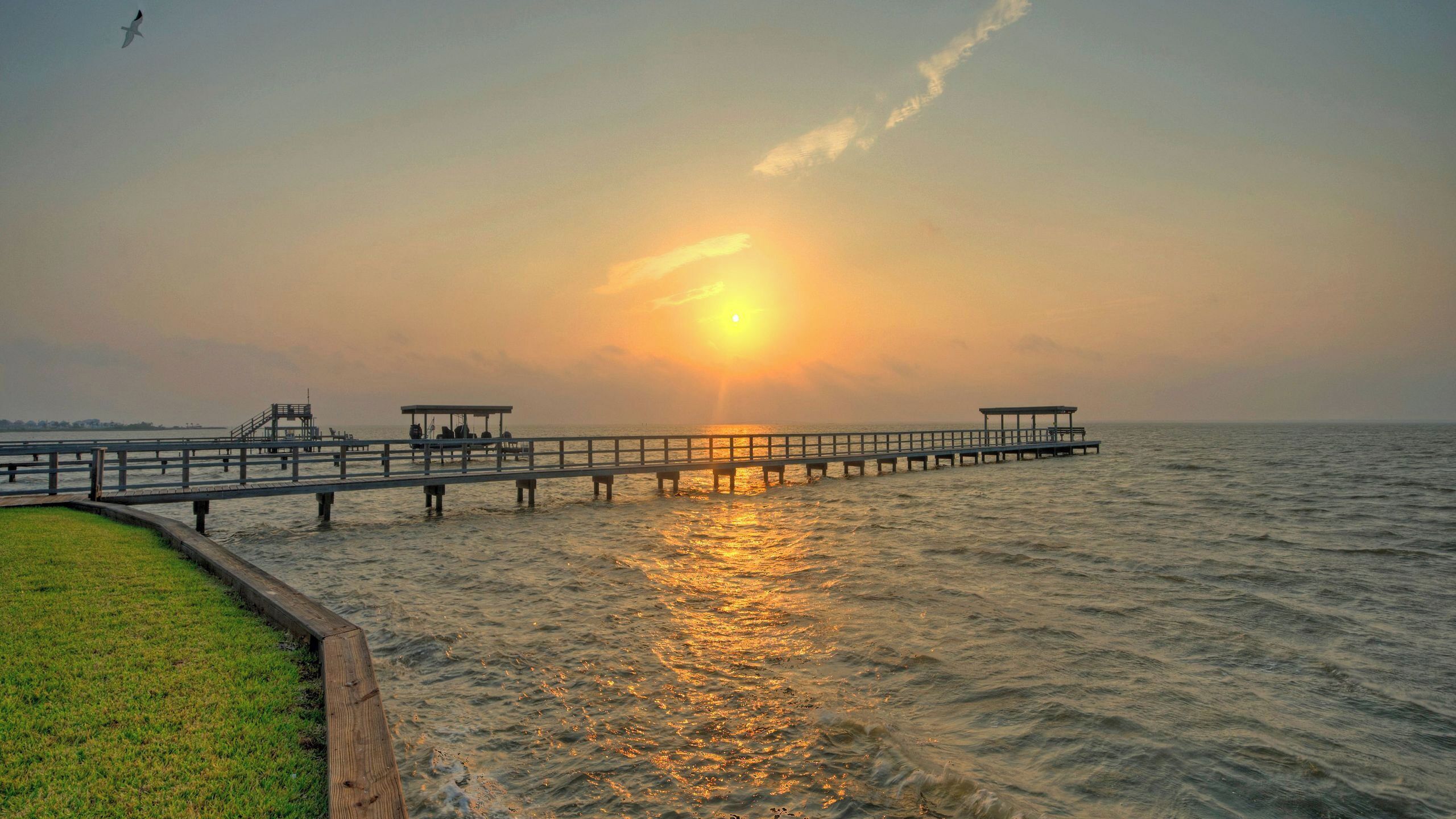 Un muelle se adentra en aguas tranquilas con un atardecer de fondo.