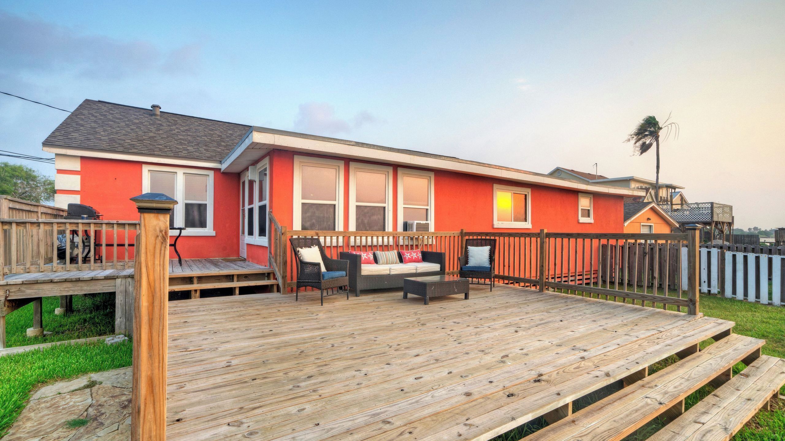 Une maison rouge avec une terrasse, un patio couvert et une cour arrière clôturée.