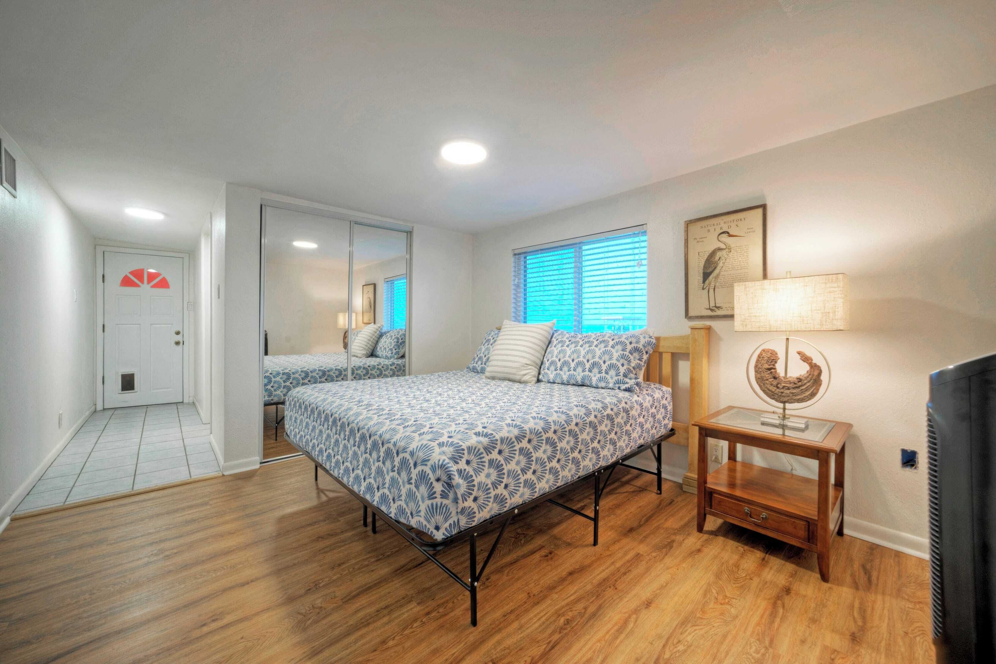 A bedroom with a bed, a mirror, a window with blinds, a lamp, and a television.