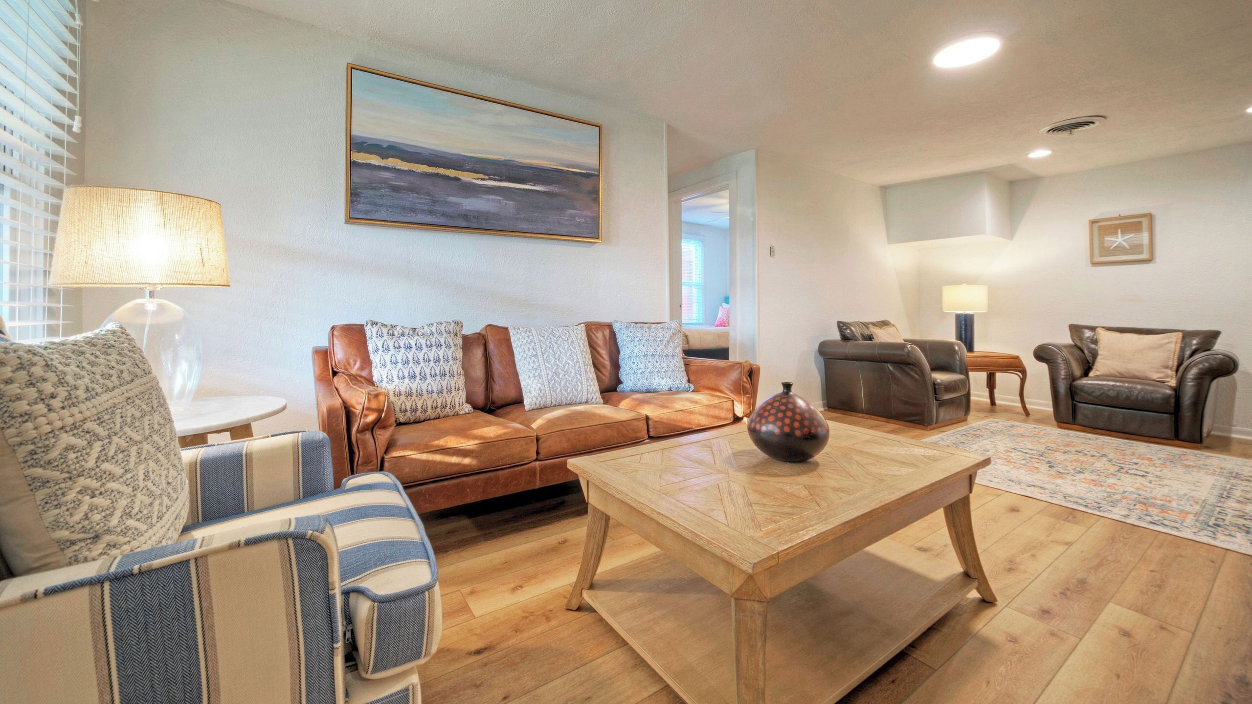 A living room with a brown leather sofa, a striped armchair, a wooden coffee table, and a painting on the wall.