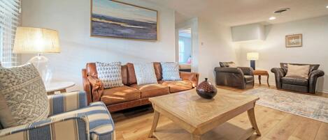 A living room with a brown leather sofa, a striped armchair, a wooden coffee table, and a painting on the wall.