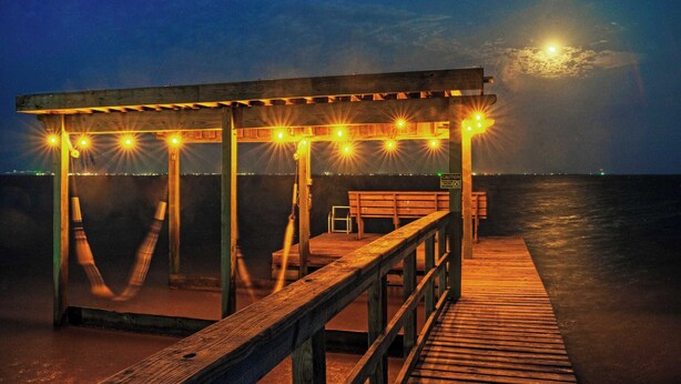 Puinen laituri, jossa on penkki ja katettu oleskelualue, joka on koristeltu valonauhoilla.