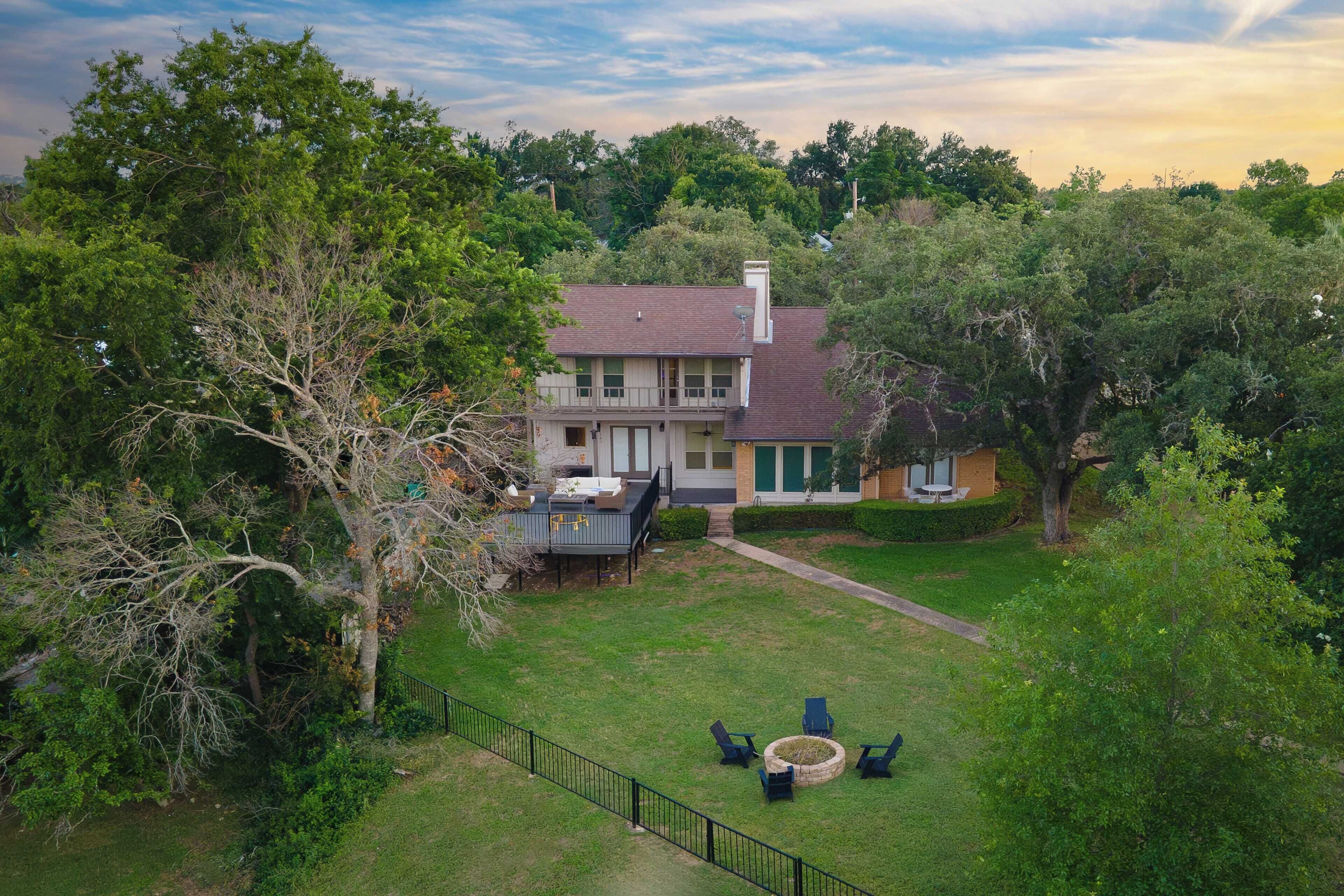 A two-story house with a deck, surrounded by lush greenery and trees.