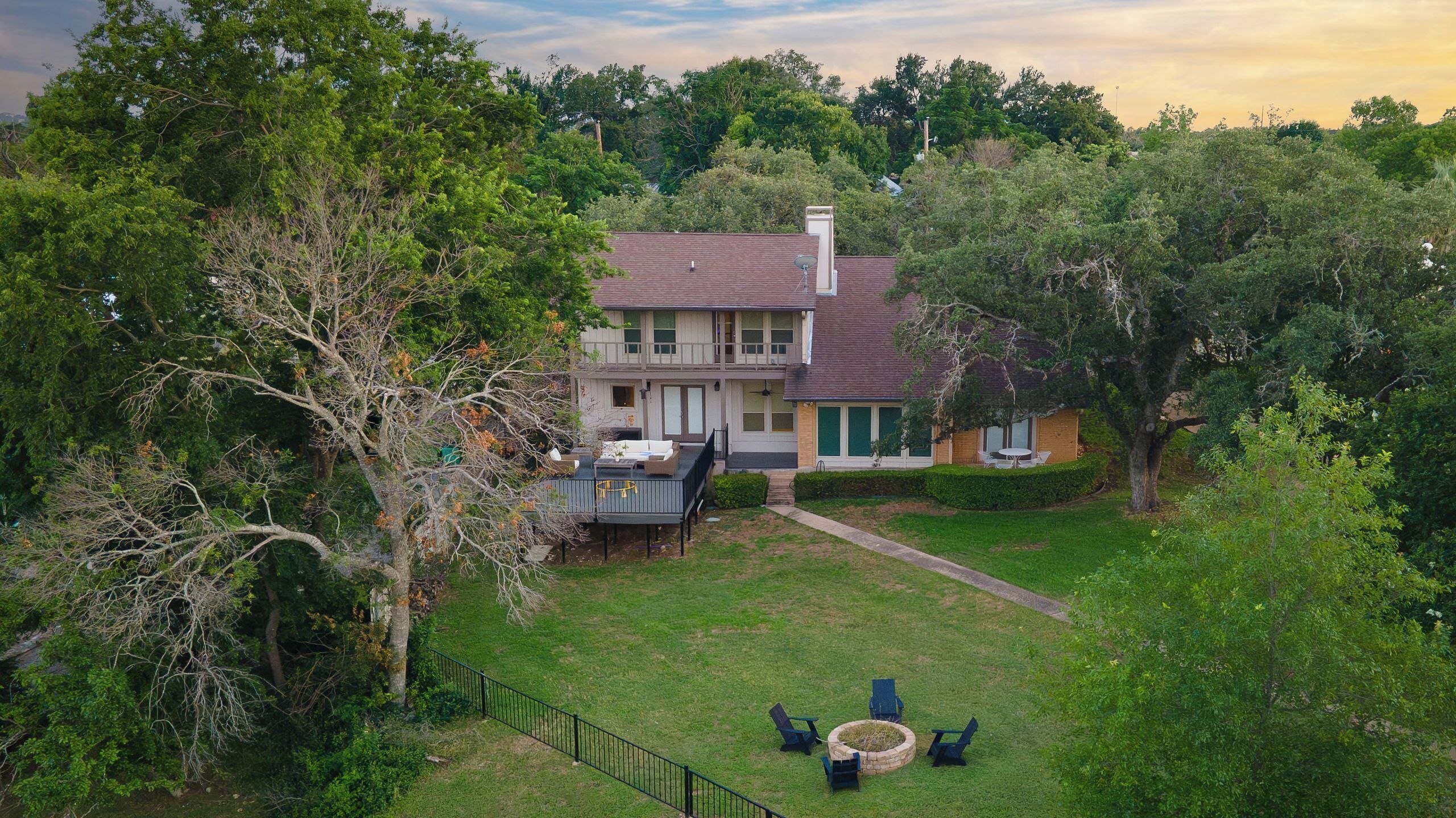 A two-story house with a deck, surrounded by lush greenery and trees.