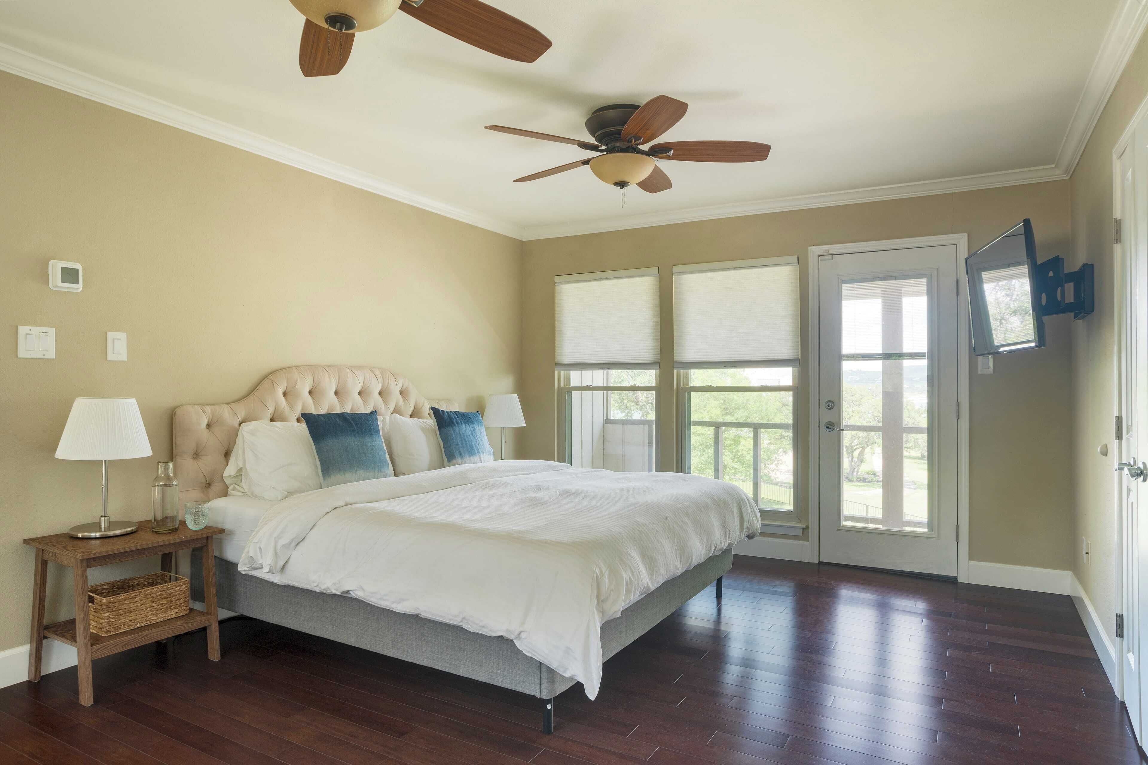 Une chambre à coucher avec un lit, des tables de chevet, un ventilateur de plafond et de grandes fenêtres.