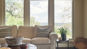 A living room with a beige sofa, patterned cushions, a marble bowl, and a potted plant by a window with a view. - Travis by Avantstay Waterfront Lake Retreat (Austin)