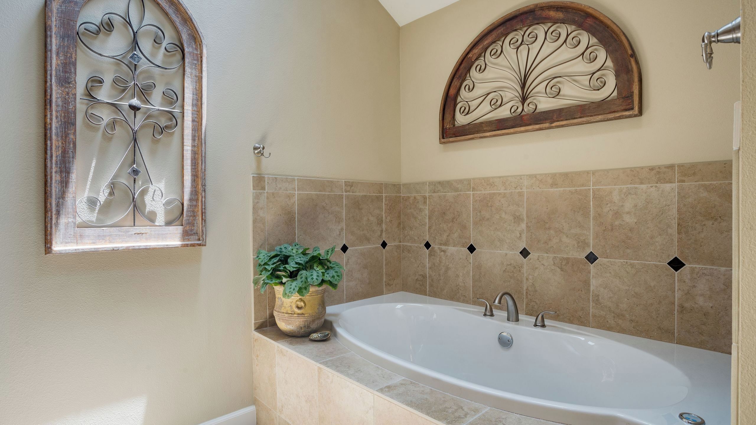 A bathroom with a bathtub, a window with decorative ironwork, and a wall-mounted decorative piece.