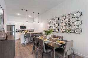 Une cuisine moderne dotée d’appareils électroménagers en acier inoxydable, un coin repas avec une grande table et des chaises, et un élément décoratif mural.