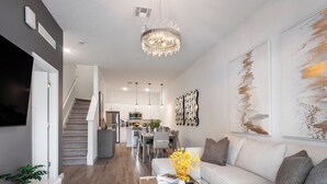 A modern living room with a white sofa, a coffee table with decorative items, a chandelier, and artwork on the walls.