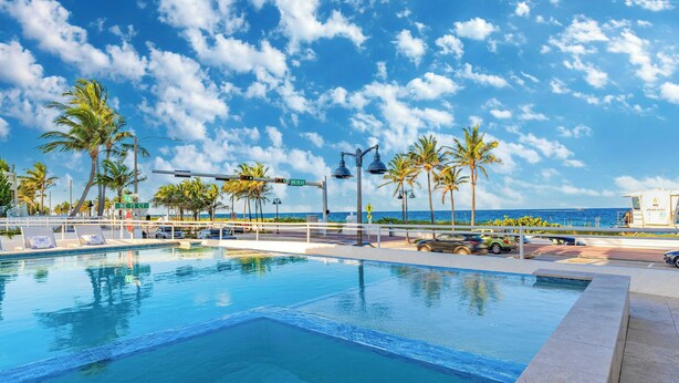 A swimming pool with lounge chairs, palm trees, and a view of the ocean.