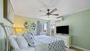 Un dormitorio con cama, ventilador de techo, televisión y obras de arte en las paredes.