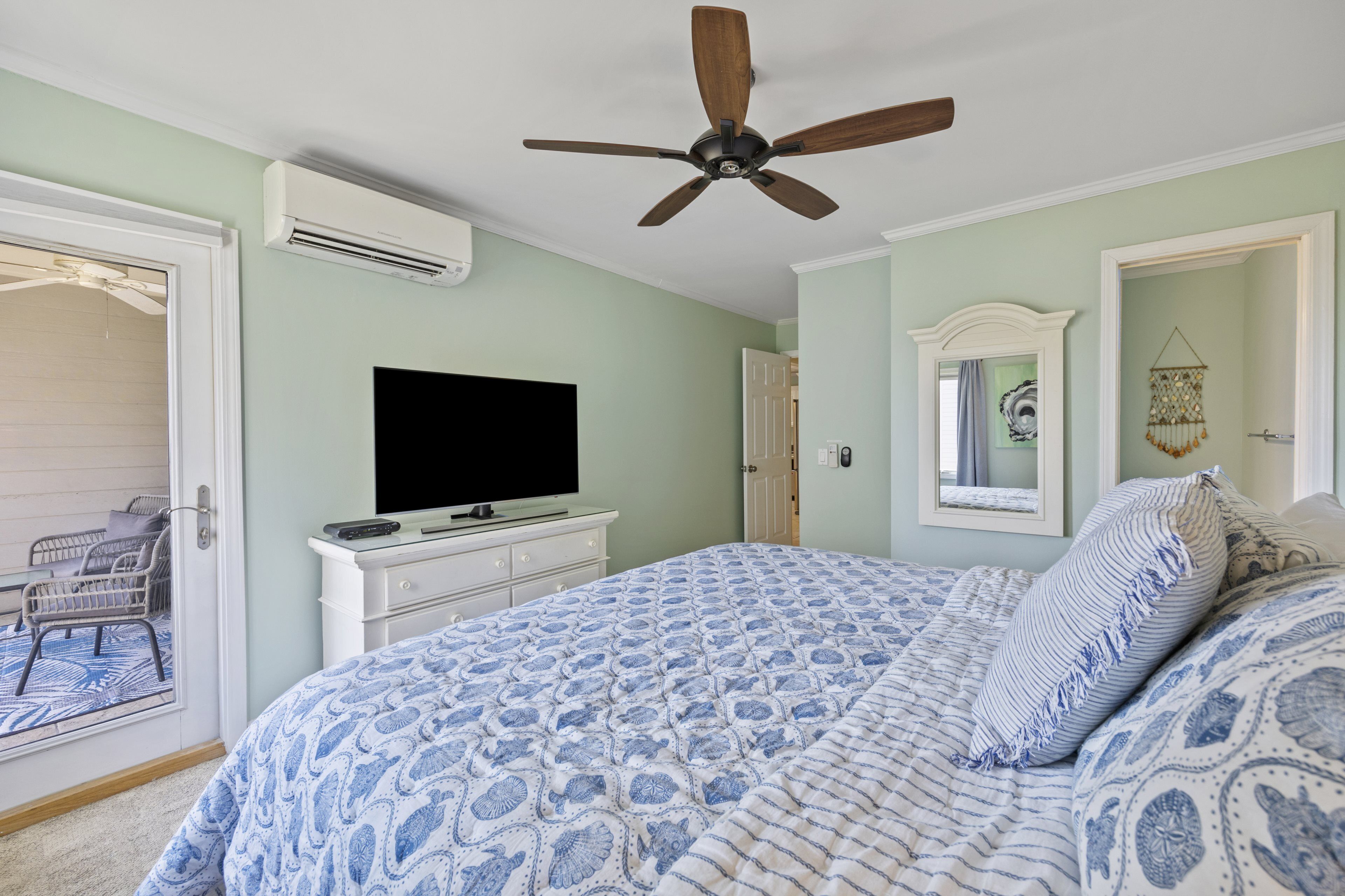 A bedroom with a bed, a ceiling fan, a TV on a dresser, and a door leading to a balcony.