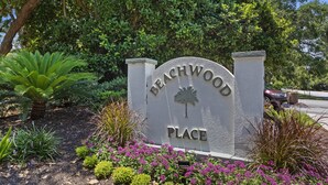Letrero de 'Beachwood Place' con un emblema de palmera, rodeado de plantas y flores.